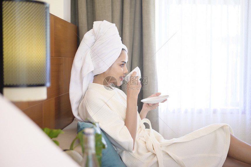 一个穿着白浴袍和毛巾的放松妇女早上喝咖啡图片