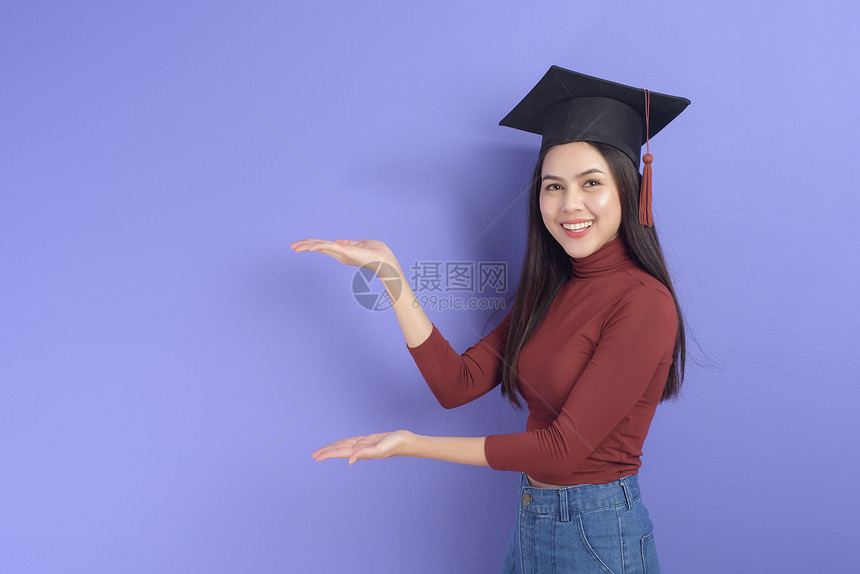 具有紫背景毕业上限的年轻大学女生的肖像图片