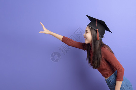 具有紫背景毕业上限的年轻大学女生的肖像高清图片