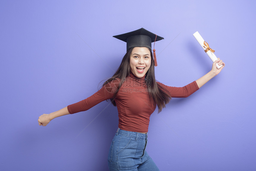 具有紫背景毕业上限的年轻大学女生的肖像图片