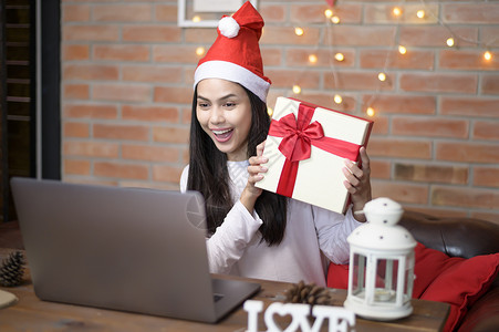 服装素材网站一位戴着红色圣诞老人帽子的微笑年轻女在圣诞节当天与家人和朋友在社交网络上进行视频通话背景