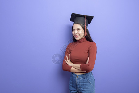 具有紫背景毕业上限的年轻大学女生的肖像图片