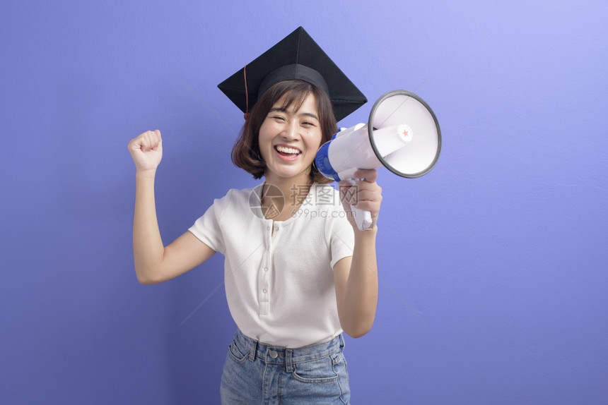 拥有扩音器孤立紫色背景演播室的亚洲毕业生学肖像图片