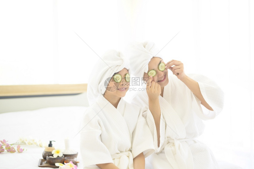 穿着白浴袍的美丽母亲和女儿快乐在卧室家庭和美容概念中戴面罩图片