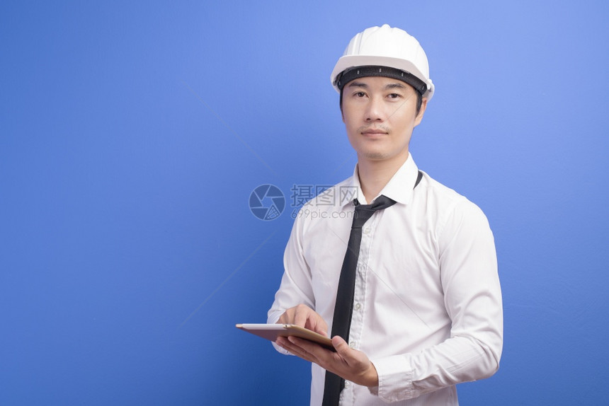 在蓝色背景制片厂上穿着白色用平板穿着白色衣服的自信男工程师的肖像图片