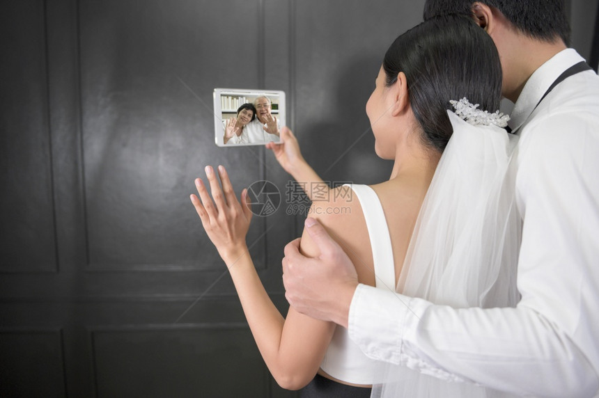 婚纱中的一对夫妇在与父母进行视频通话时图片