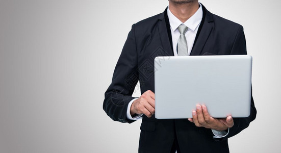 商人站立姿势手持笔记本电脑在灰色背景上被孤立图片