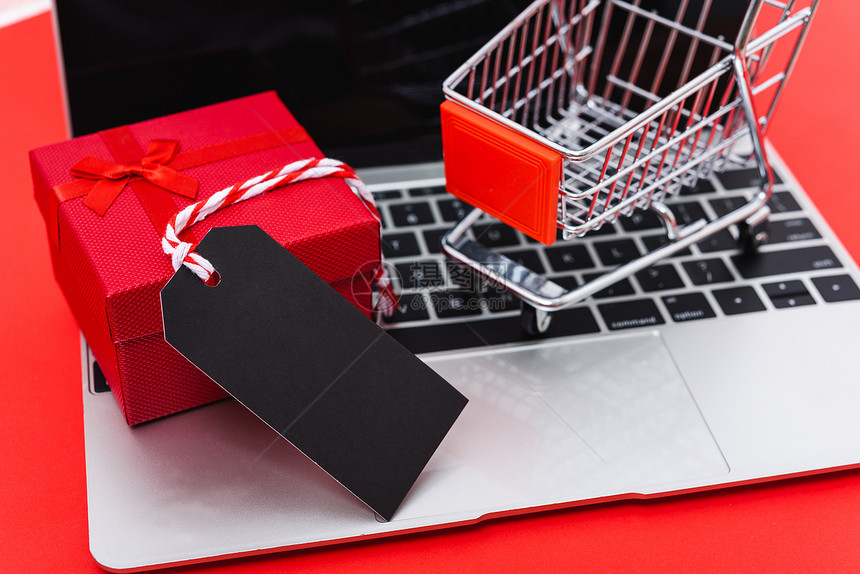 网上购物营销空白黑标签礼品箱和在红背景手提笔记本电脑上用手提购物的工作场所顶层图像礼品箱和手推购物并有供使用的复制空间图片