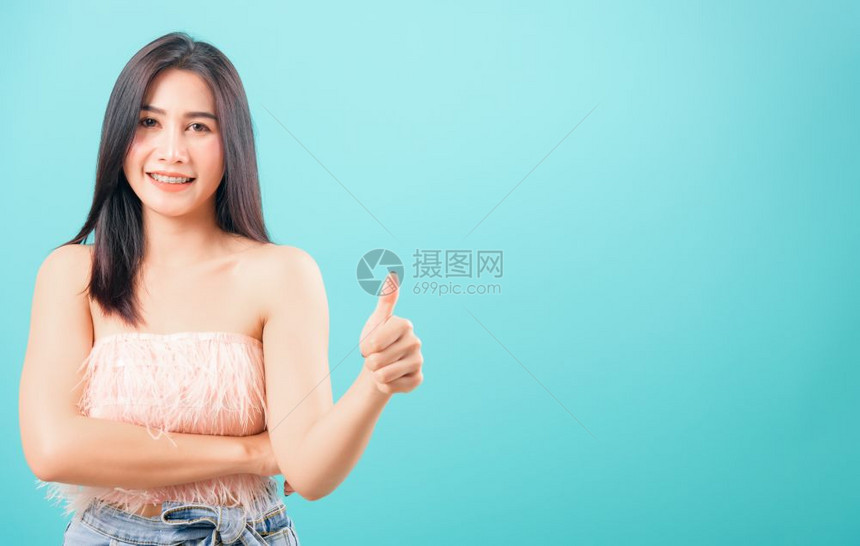 脸貌鲜明的亚洲美丽女微笑着她举起拇指仰望着蓝色背景的相机复制文本空间图片