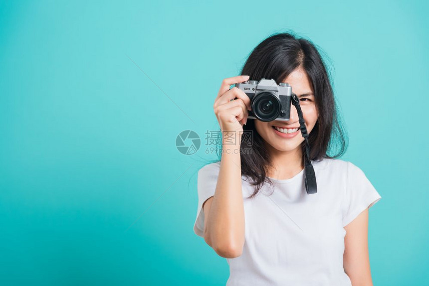 旅游者快乐的亚洲美丽年轻女穿着夏帽微笑拿无照相机站在无的夏帽拍摄蓝背景影棚的照片复制文本空间图片