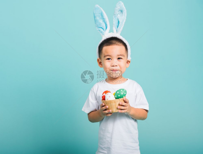 亚洲可爱的小孩男微笑带着兔子耳朵和白色T恤衫站在篮子上着图片