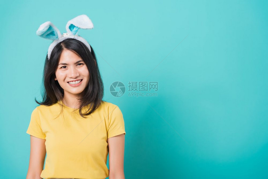 亚洲美丽笑着白牙的年轻女身穿黄色T恤衫站在兔子耳朵边立图片