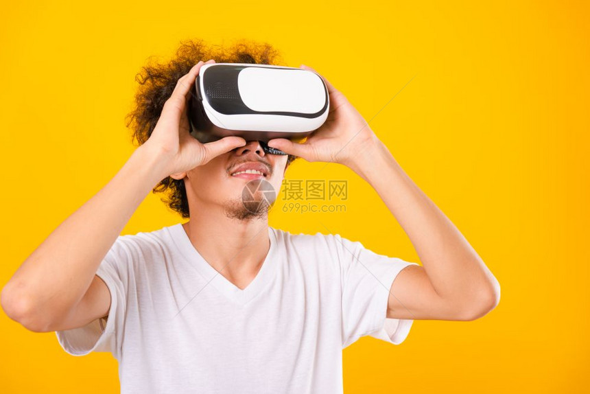 亚洲长着卷发的帅男子使用虚拟现实头耳机或黄色背景的VR玻璃分离器图片