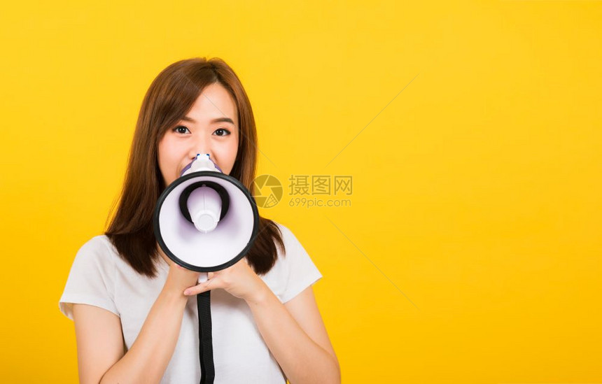 亚洲快乐的肖像亚洲美丽可爱的年轻少女站立在发布公告信息在扩音器中尖叫看着摄像机被孤立影棚拍黄色背景带有复制空间图片