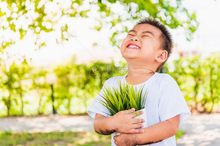 世界环境日与拯救世界概念亚洲可爱的快乐小男孩手在绿色花园背景下在白锅上抓着小树图片