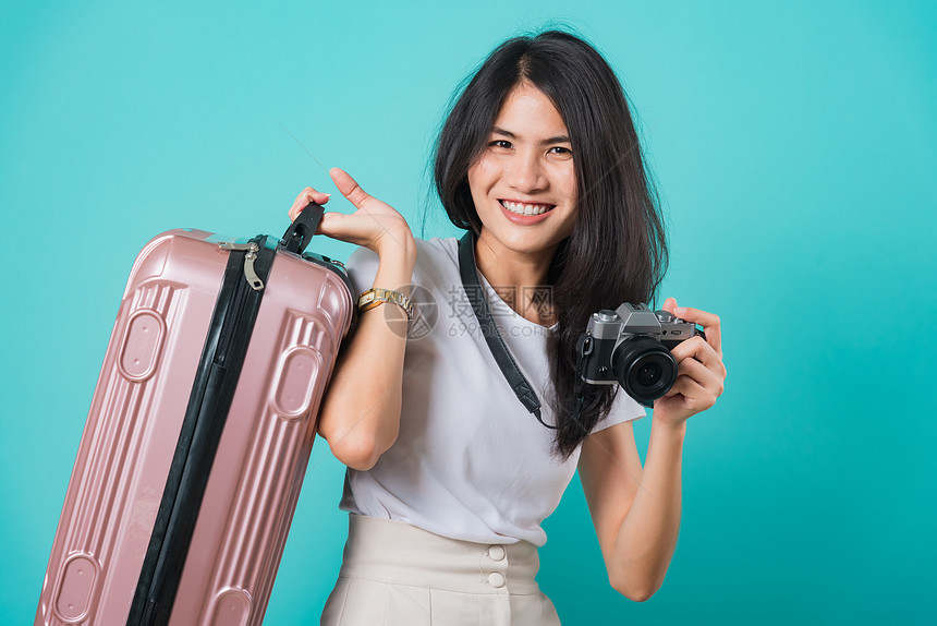 旅行者快乐的亚洲美丽年轻女站着穿白色T恤衫假期旅行概念她拿着手提包照片不相机在摄影棚拍蓝底照片图片