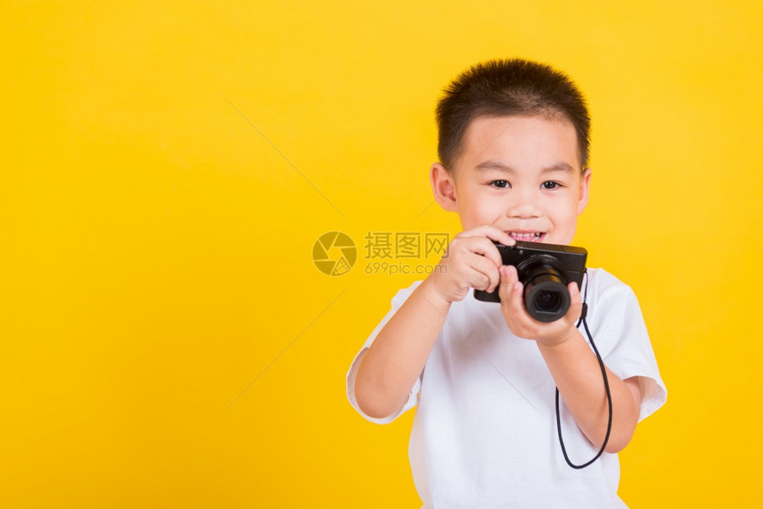 亚洲泰国快乐的肖像可爱的小男孩拿着摄影像头拍着照片摄影棚拍以黄色背景与复制空间隔绝图片