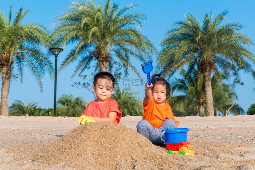 亚裔泰国人快乐可爱的小快乐弟和妹两个孩子的和两个孩子在夏日用复制空间在户外热带海滩用沙子挖玩耍具图片