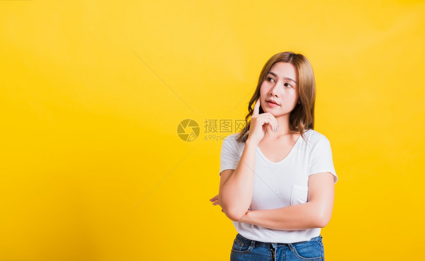 身着白T恤的亚洲美丽泰国年轻女站在下巴着放松思考一些关于问题工作室拍摄的片段孤立在黄色背景上带有复制空间图片