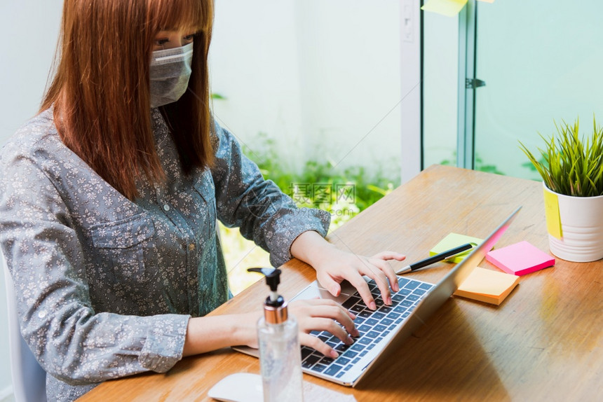 亚洲商业美丽的年轻女在家中办公室工作他戴着保护面罩消毒胶和剂并同时使用笔记本电脑在线检疫疾病冠状毒或COVID19图片