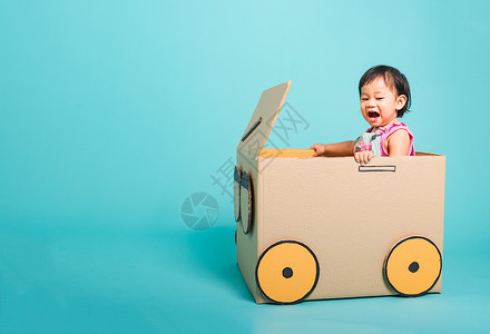 快乐的亚洲女婴在驾驶车时微笑由纸箱想象力暑假旅行概念蓝背景摄影棚拍图片