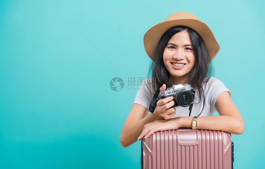 旅行者快乐的亚洲年轻美女穿着白色T恤衫假期旅行概念她拿着李袋照片不摄影机在棚拍蓝底照片图片