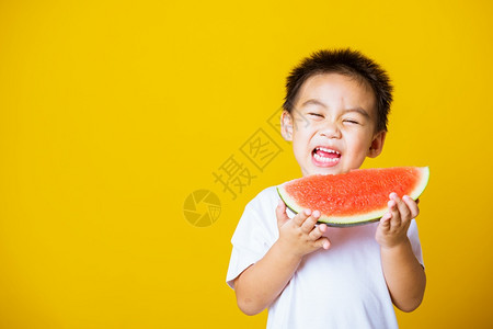 快乐的亚洲儿童或孩子可爱的小男孩笑玩着切开西瓜新鲜食物拍片室摄孤立在黄色背景上健康食物和夏季概念背景图片