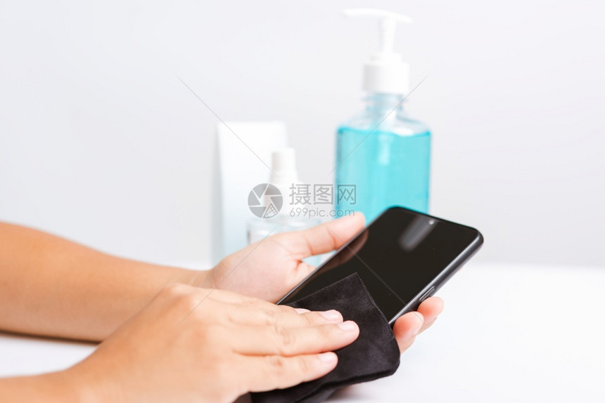 亚洲青年妇女将新闻撒布机净化剂酒精喷洒液射到智能移动电话清洗卫生预防COVID19或冠状保护概念孤立的白种背景图片