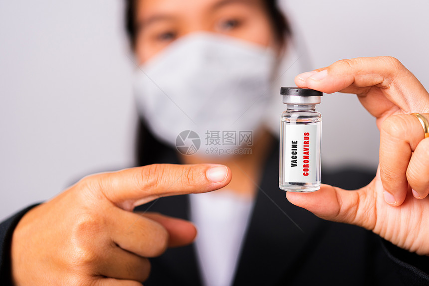 身穿外科保护布面罩的亚洲女医生对抗冠状她指针的氨水瓶疫苗集中在玻璃标签上摄影棚拍孤立的白色背景COVID19图片