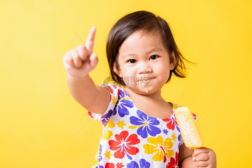 快乐的亚洲小婴儿或孩可爱的女快乐肖像笑有吸引力的小女孩笑穿着鸡样衬衫并吃甜木冰淇淋摄影棚拍着黄色背景夏季概念图片