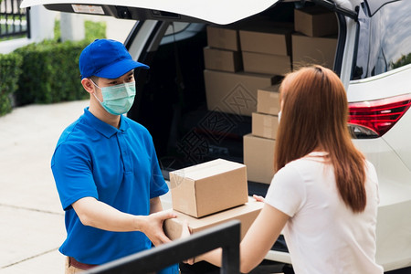 箱套期保值亚洲青年送货员在线采购亚洲青年送货员给他包裹邮箱保护面罩和女服务客户在前家门接受箱套根据宵禁大流行的科罗纳COVID19背景