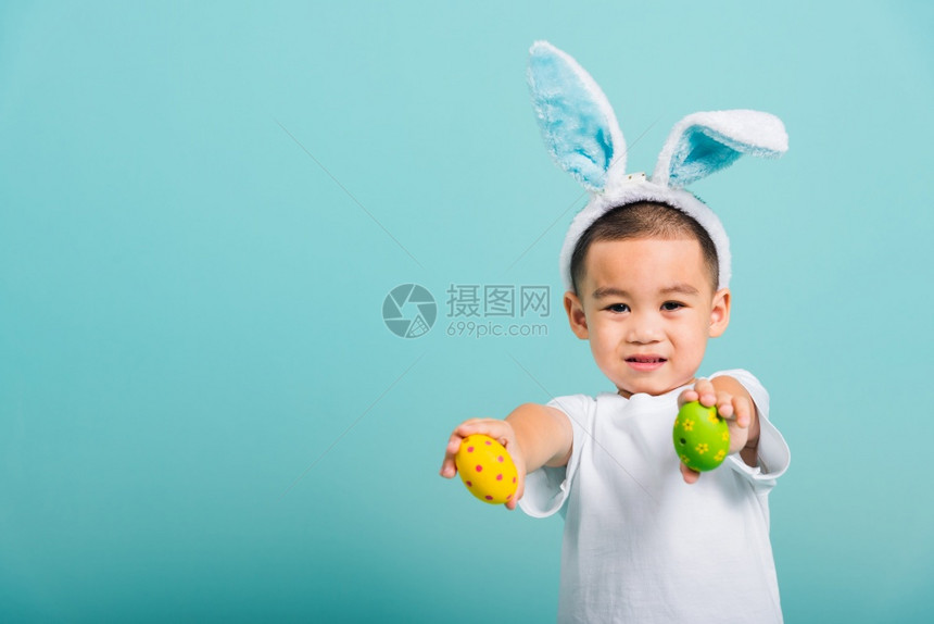 亚洲可爱的小孩男微笑戴着兔子耳朵和白色T恤衫站着手握图片