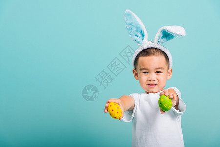 亚洲可爱的小孩男微笑戴着兔子耳朵和白色T恤衫站着手握图片