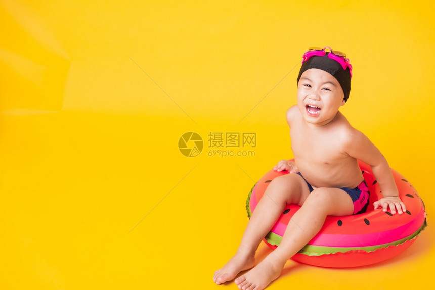 暑假概念肖莱特亚洲快乐可爱的小男孩穿着护目镜泳衣握着海滩西瓜充气环基德玩得开心坐在充气机里工作室拍着孤立的黄色背景图片