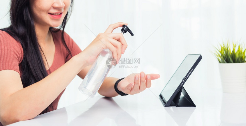 在家庭办公室工作的亚洲商业年轻女人在前台平板电脑上用洗净剂凝胶清她的洁手他隔离了冠状或COVID19图片
