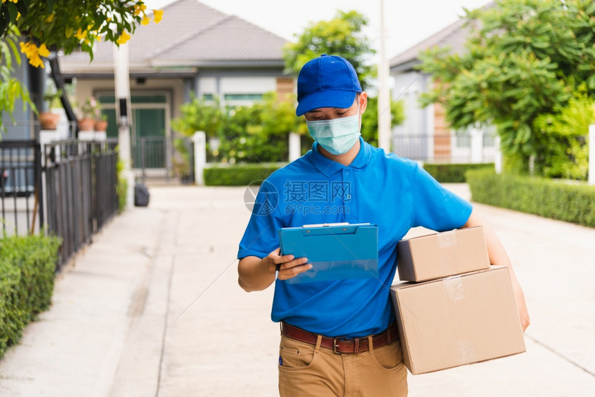 亚洲青年送货员信使携带包裹邮箱保护面罩服务在宵禁大流行的COVID19下步行寻找客户住家地点图片
