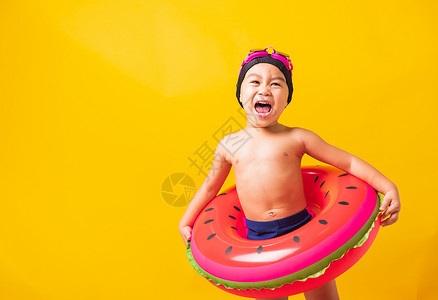 亮黄色的泳衣暑假概念肖莱特亚洲快乐可爱的小男孩穿着护目镜和泳衣抓着西瓜的充气环基德在暑假玩得开心工作室拍摄孤立的黄色背景背景