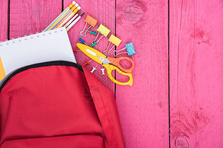 以粉红木背景为教育的儿童返回学校概念的红色背包图片