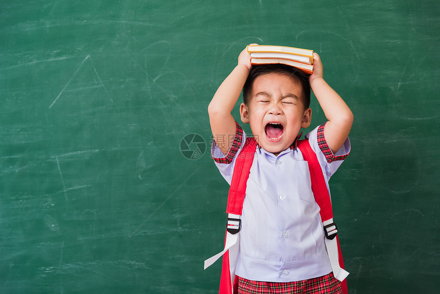 快乐的亚洲可爱小孩男从幼儿园穿着校服拿书包和本头在绿色学校黑板上微笑第一次到学校教育概念图片