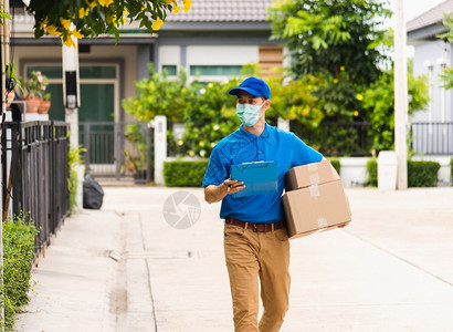 冠状病毒信使亚洲青年送货员信使携带包裹邮箱保护面罩服务在宵禁大流行的COVID19下步行寻找客户住家地点背景