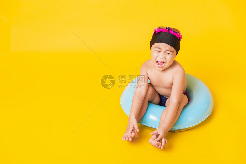 暑假概念肖莱特亚洲快乐可爱的小男孩穿着护目镜泳衣握着海滩蓝色充气环基德玩得开心坐在充气机里工作室拍着孤立的黄色背景图片