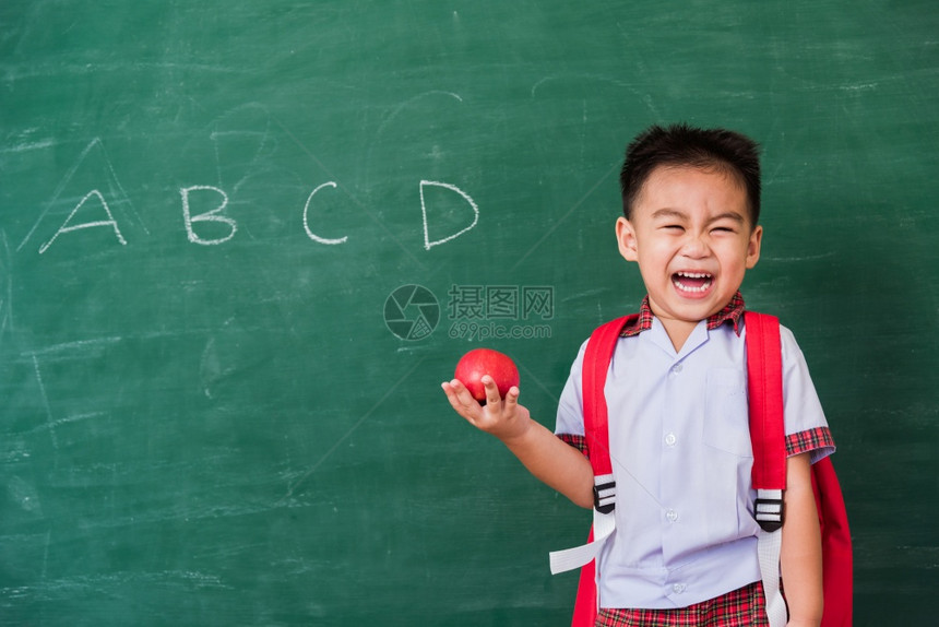 可爱小男孩穿着校服站在绿色校黑板上微笑图片