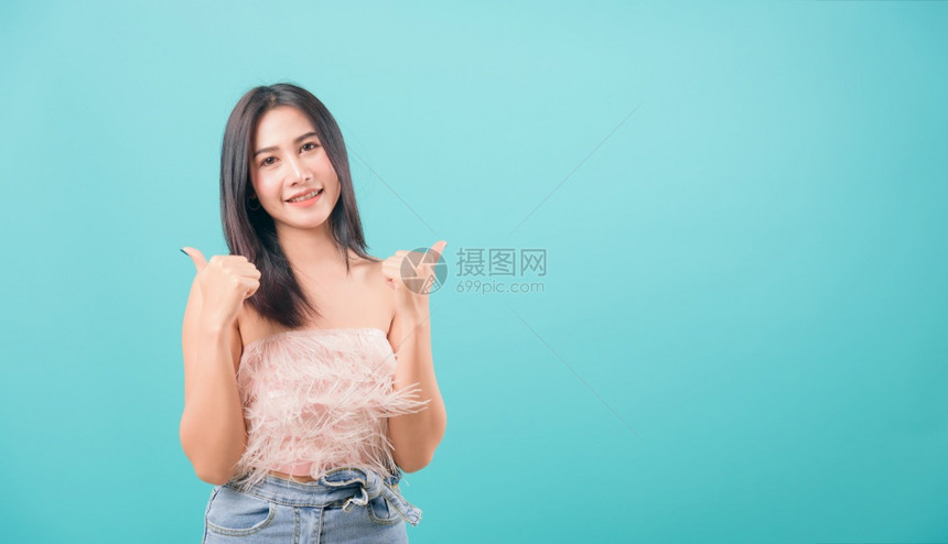 亚洲快乐肖像美丽的年轻女站在微笑的中手举起拇指标志寻找蓝色背景的摄像头与复制文本空间隔绝图片