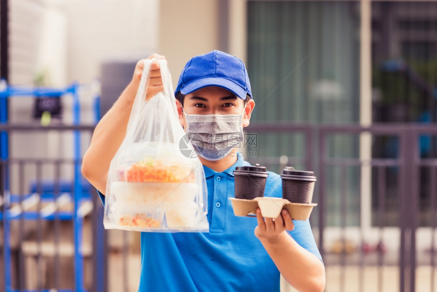 身着蓝制服的亚洲青年送货员戴面罩提供杂货服务根据流行冠状在前屋提供大米食品盒塑料袋和咖啡回到新的正常概念图片