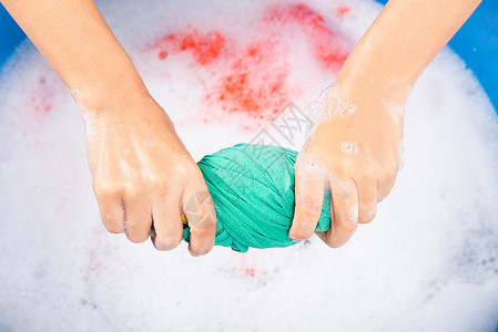 彩弹射击紧闭的亚洲年轻女在盆地用手洗彩衣物女用洗涤剂挤的湿布有水中肥皂泡工作室拍摄背景洗衣概念背景