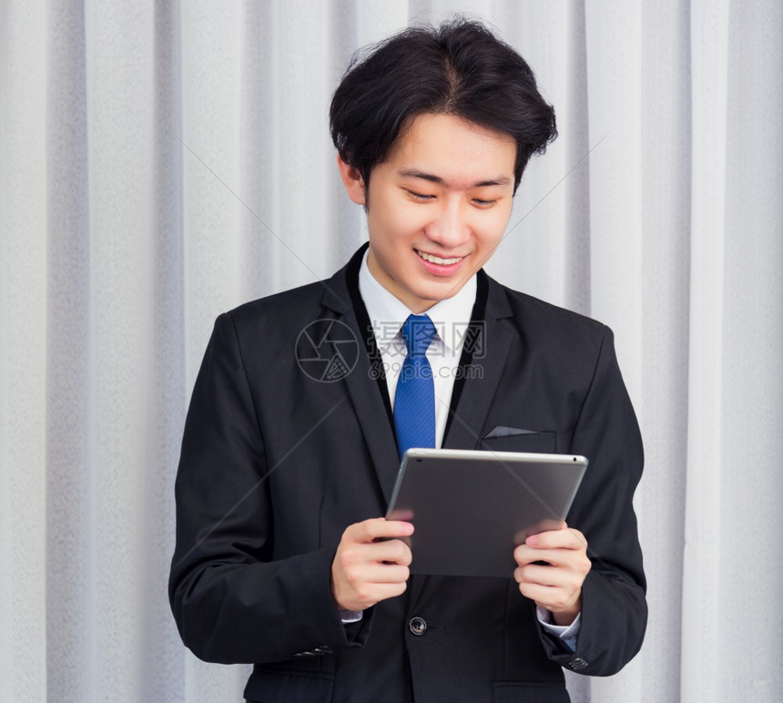 在家工作亚洲青年商人穿西装时视频会议电话或当面微笑使用智能数字平板电脑在家庭办公室触摸屏幕寻找平板电脑图片