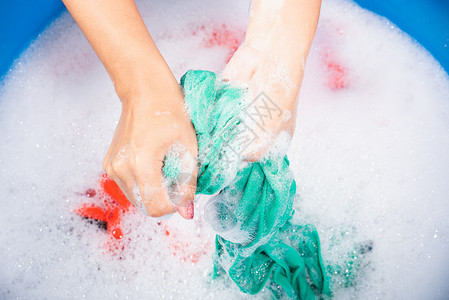 泡沫棉近身的亚洲年轻女子在盆地用手洗彩色衣服带涤剂有肥皂泡水工作室拍摄背景洗衣服概念背景
