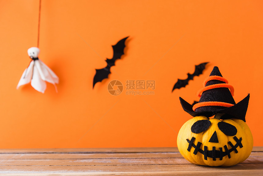 可爱的万圣节装饰派对可爱南瓜鬼祟的灯笼脸顶戴帽子黑蜘蛛和蝙蝠在木板桌上摄影棚拍以橙色背景隔离快乐假期概念图片