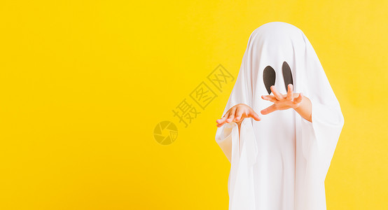 万圣节鬼魂有趣的万圣儿童概念关闭一个可爱的小孩穿着白色服装的神圣的鬼魂吓坏了摄影棚拍孤立的黄色背景背景