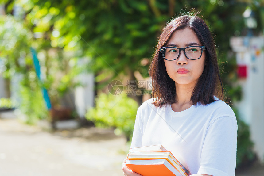 亚洲年轻美丽的女子肖像戴着眼镜的微笑牙齿套在上笑户外她手持教育书籍医学和牙概念图片